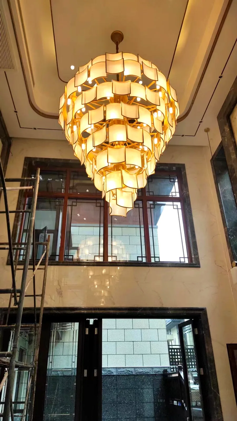 Double-height villa foyer — silk and copper tiered chandelier during installation